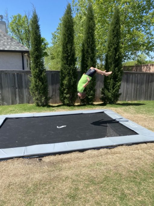 child doing a trick on a gray rectangular inground trampoline