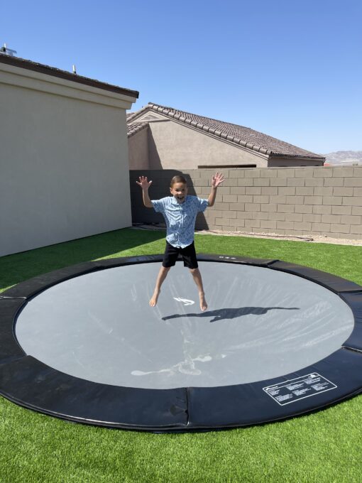 child jumping on a black round inground trampoline
