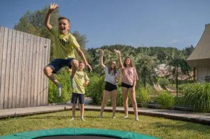 A group of children joyfully jumping on a trampoline, showcasing their excitement and energy in a sunny outdoor setting.