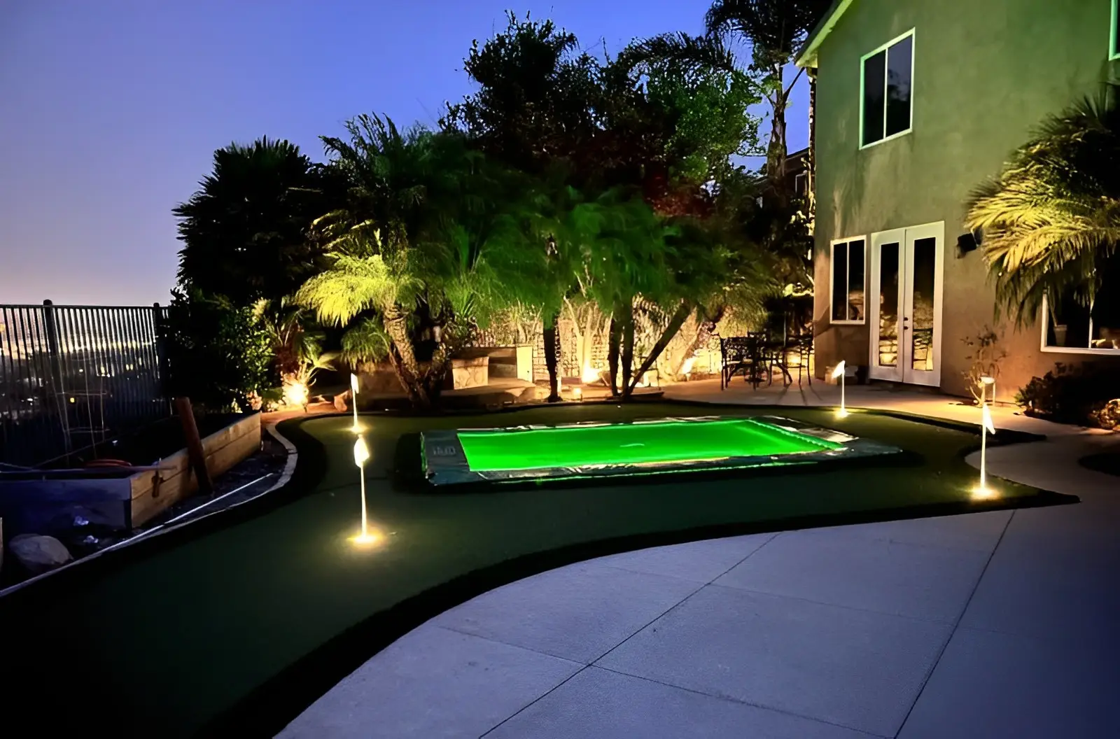 12ft Round Akrobat Primus Flat In-Ground Trampoline - Black (Black Pad with Grey Jump Mat) 6 A tranquil nighttime backyard scene showcasing a glowing pool, with ambient lighting enhancing the peaceful atmosphere.