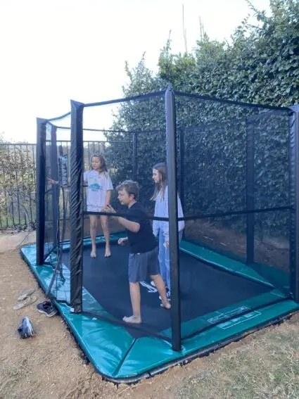 In a vibrant backyard, two children are happily playing on a trampoline, enjoying a sunny day filled with laughter.