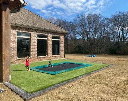 A young child happily jumping on a trampoline in a sunny backyard filled with green grass.