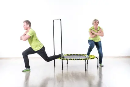 A lively scene of two people jumping on a trampoline within a spacious, white room, emphasizing movement and excitement.