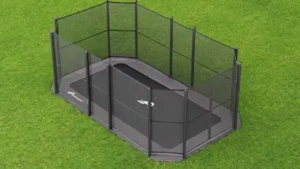 A black trampoline sits on green grass, surrounded by a vibrant green fence.