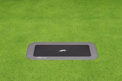 A vibrant trampoline set in the center of a lush green grass field, inviting play and outdoor fun.