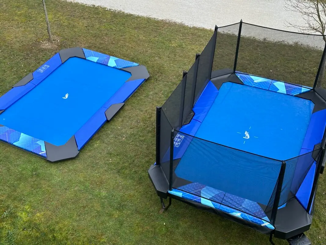 Two blue-matted trampolines positioned on a grassy area, inviting for recreational activities and outdoor fun.
