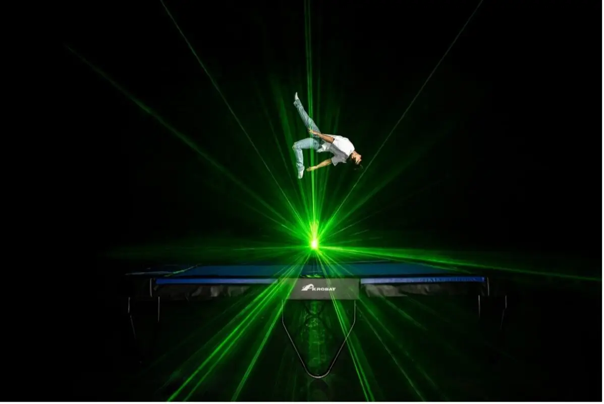 A man performs an impressive trick on a trampoline illuminated by vibrant green light.