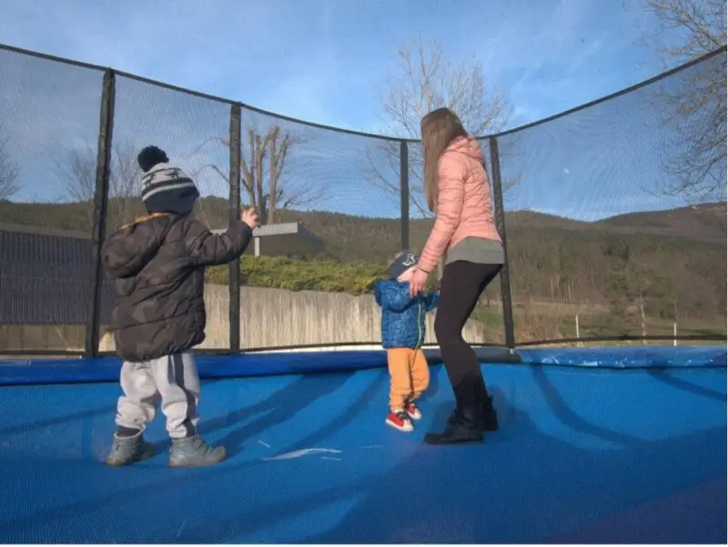 A-woman-and-two-children-joyfully-playing-together-on-a-trampoline-in-a-sunny-outdoor-setting.